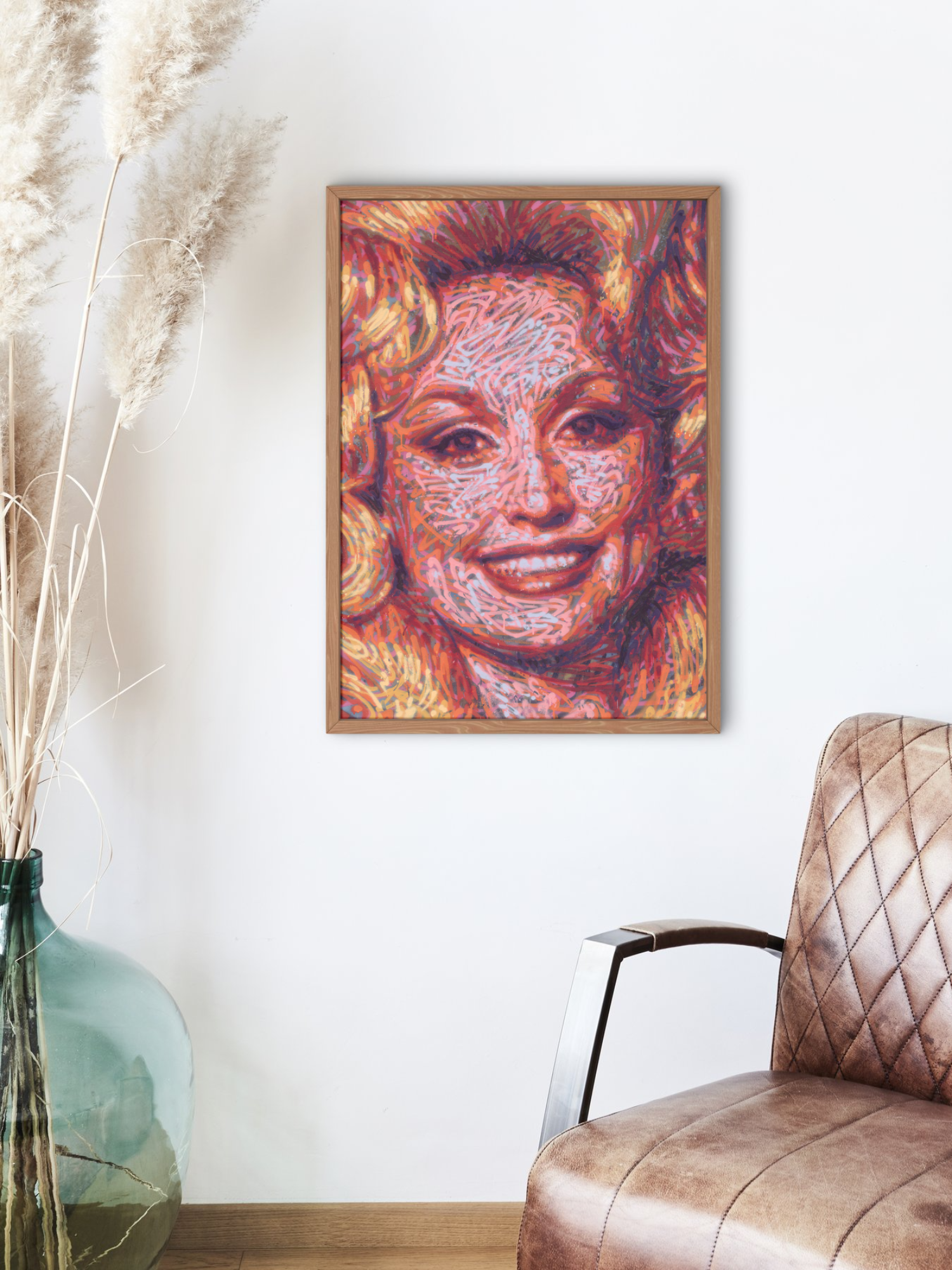 Mockup of a graffiti spray can portrait by Ben Jay of Blank Space Removal of a closeup of Dolly Parton's face and bouffant hair, in a wooden frame hung on a white wall with a chair and vase nearby.