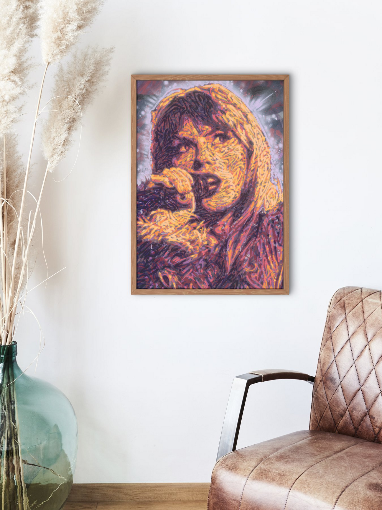 Mockup of a graffiti spray can portrait by Ben Jay of Blank Space Removal of Taylor Swift holding a microphone, in a wooden frame hung on a white wall with a chair and vase nearby.